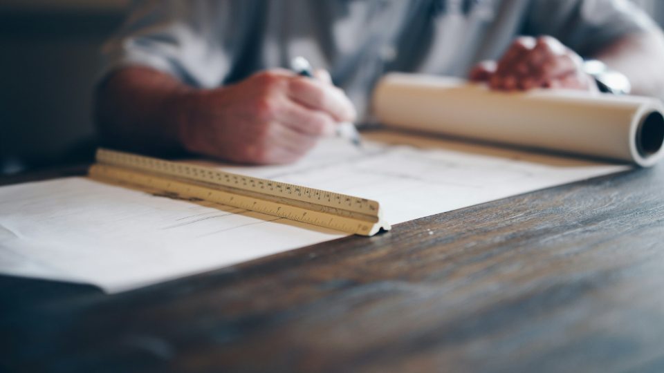 Manos dibujando los planos de una vivienda sobre una mesa de madera